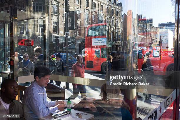 Lunchtime diners chat and enjoy spring sunshine in a Pret-a-Manger restaurant chain in central London. Outside, city pedestrians walk-by amid the...