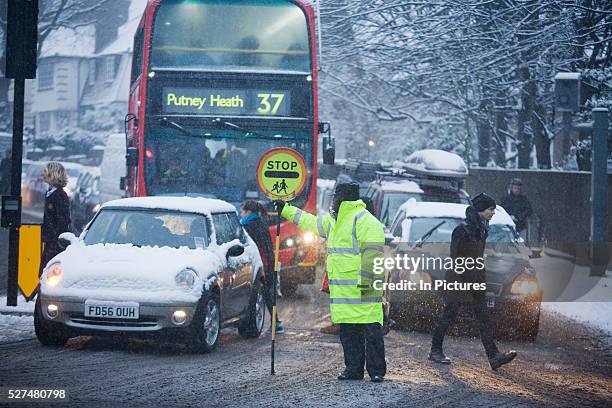 In the morning rush-hour, a busy road junction is seen during a snow-shower as traffic builds up at traffic lights and pedestrians to and fro in...