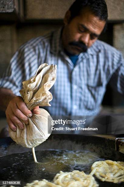 Man squeezes batter from a cloth to make jalebis at the Old and Famous Jalebi Wala . Delhi, India