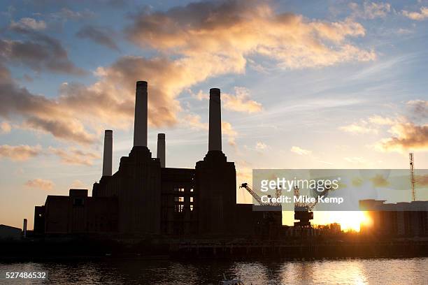 The iconic Art Deco Batersea Power Station at the edge of the River Thames at sunset. The four towers silhouetted against the sun and clouds.