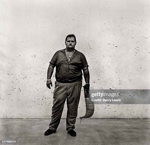 Cuban Jai Alai stands ready with his woven basket glove which he will use to hurl a puck hard against a wall and into the glove of his opponent. The...