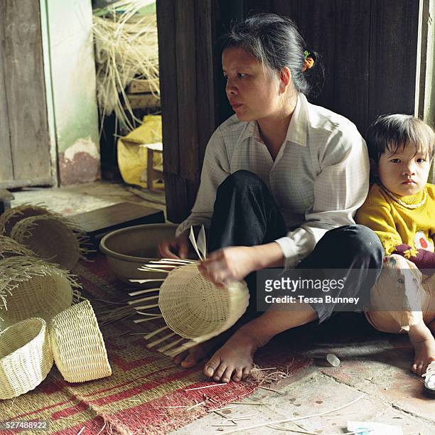 Young girl sits with her mother while she weaves baskets, Luu Thuong, 'Te' grass weaving village, Ha Tay province, Vietnam. With Vietnam's growing...
