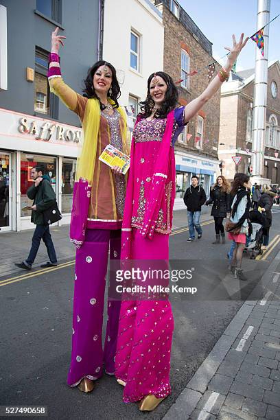 Stilt walkers at an Asian street food festival on Brick Lane, London, JUK. Dressed in pink and yellow sari material these women on stilts pose for a...