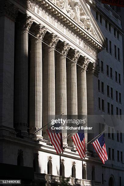 Classical pillars and American flag hanging in front of the New York Stock Exchange on Wall Street, Lower Manhattan. This famous street symbolises...