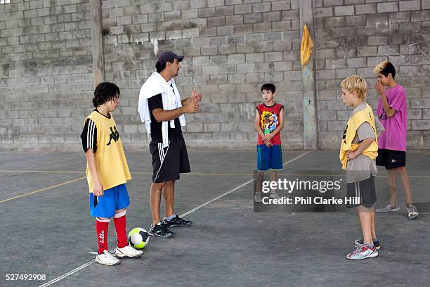 Young boys men teenagers playing football on a concrete pitch court, at La Casita home for disadvantaged or recovering street children, Buenos Aires,...