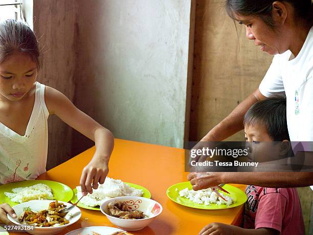 Imelda Esgana, fish vendor eating lunch at home with her two youngest children, Talisay, Bantayan Island, The Philippines. Every morning at 7 am...