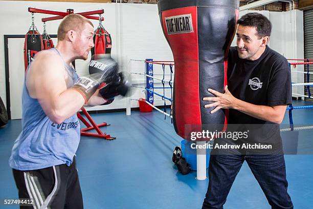 Two men boxing training also known as sparring using a heavy bag in the gym of Empire Fighting chance. Bristol, UK