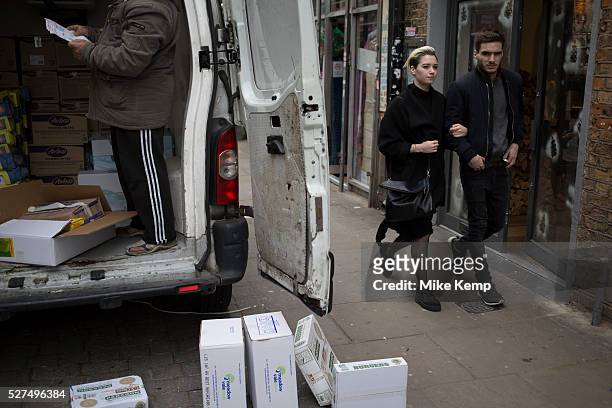 Stylish young couple pass a delivery van dropping off food items on Brick Lane in the East End of London, UK. This area is particularly know for it's...