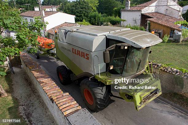 Claas combine harvester edges slowly through rural hamlet in Langlade, Charente-Maritime region, France. Between stone walls and the homes of local...