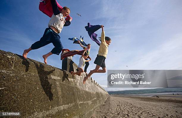 Four children leap out into the wide blue yonder on a beach in Whitley Bay, England. Jumping at a height from a sea defence wall, the kids all hold...