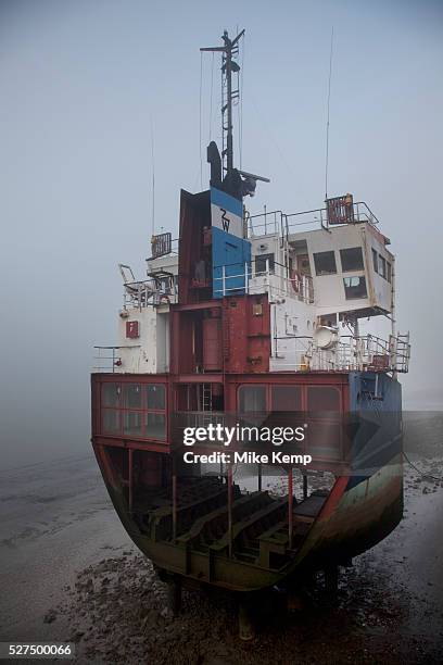 Thick fog obscures an old section of a large ship which sits in the muddy banks at low tide in London making a peaceful yet eerie landscape...