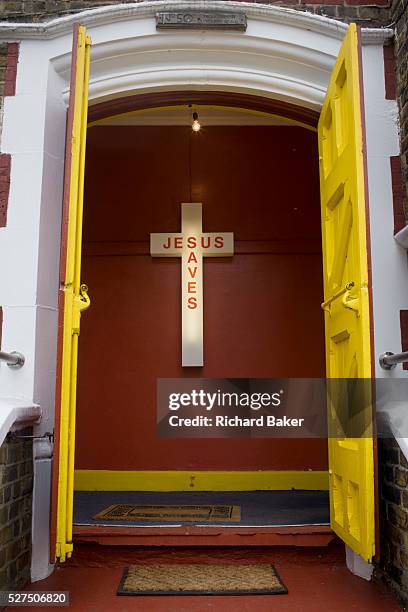 Jesus Saves neon sign in the entrance of an evangelical church in Peckham, south London. The yellow doors at the top of steps with two doormats are...