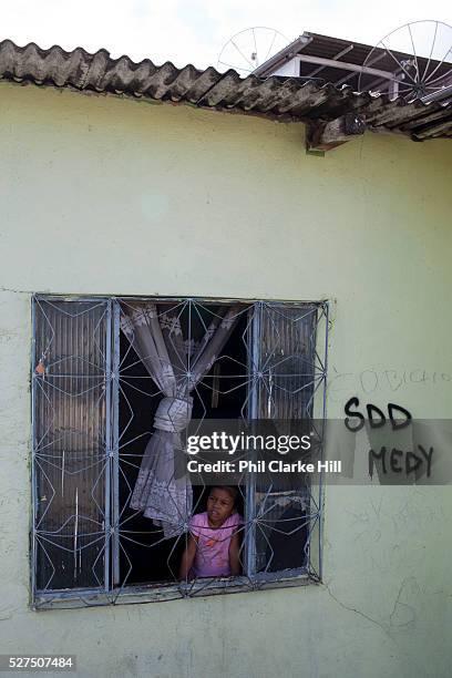 Young small girl standing in a window with grafitti next to it, in Vila Valquiere, West Zone Zona Oueste, Rio de Janeiro