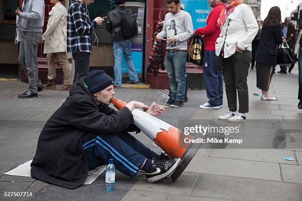 Homeless man busking to make a little money by making music with his voice through a traffic cone on a busy Oxford Street in London, amidst the...