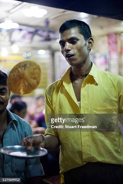 Waiter flips a cooked paratha on a plate at Parawthe Wala restaurant in Old Delhi, India The parantha is an Indian fried bread, folded and filled...