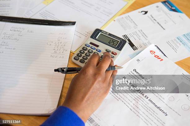 Young lady sits at her kitchen table at home checking over the household bills. Dealing with debt. Household utility bills making it difficult for a...