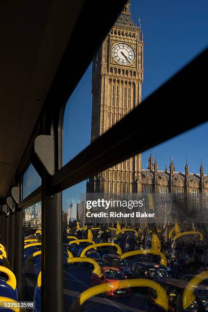 Parliament's Big Ben is seen through the top deck window of a London double-decker bus. Its yellow seating handles are seen as reflections as traffic...