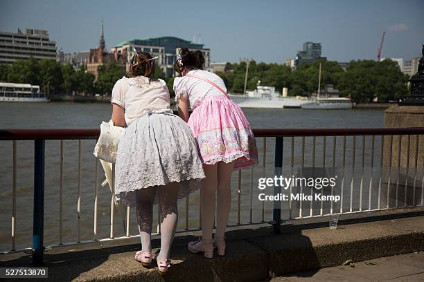 Two girls wearing Lolita dresses lean over the barrier over the River Thames on the South Bank, London, UK. Lolita fashion is a subculture...