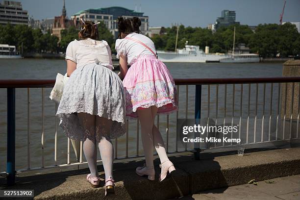 Two girls wearing Lolita dresses lean over the barrier over the River Thames on the South Bank, London, UK. Lolita fashion is a subculture...