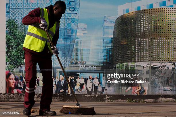 Utopian view of a London street sweeper brushing the street in front of a hoarding showing aspiration and consumerism of nearby Westfield City...