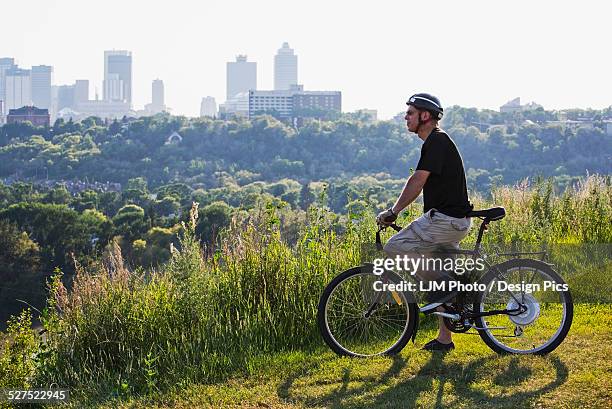 man riding his electric bicycle with edmonton city skyline in the background - edmonton stock pictures, royalty-free photos & images