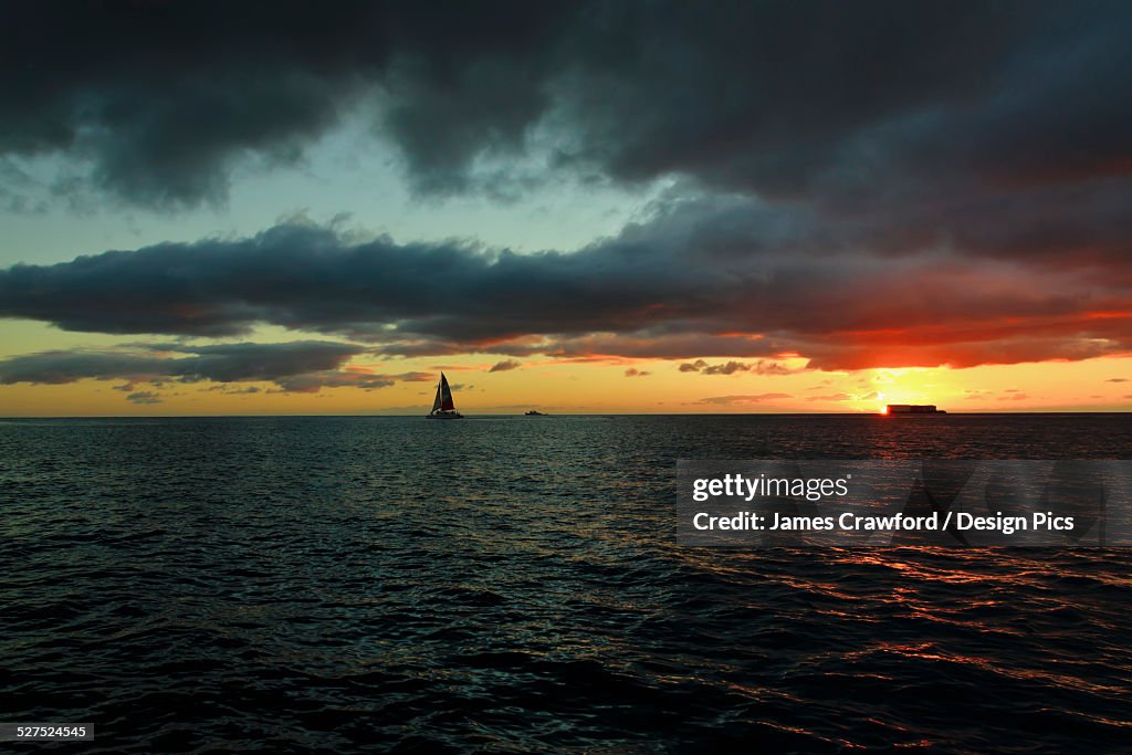 A sailboat on the ocean water off the coast of Waikiki at sunset