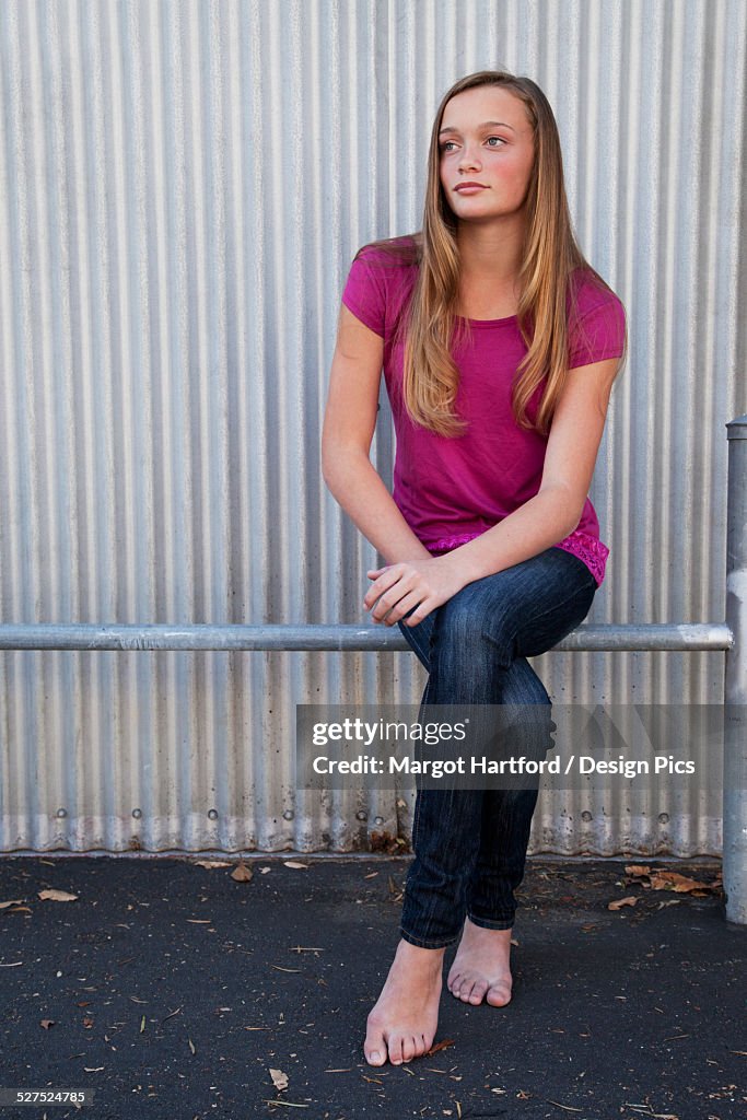 A girl sitting on a metal rail in bare feet