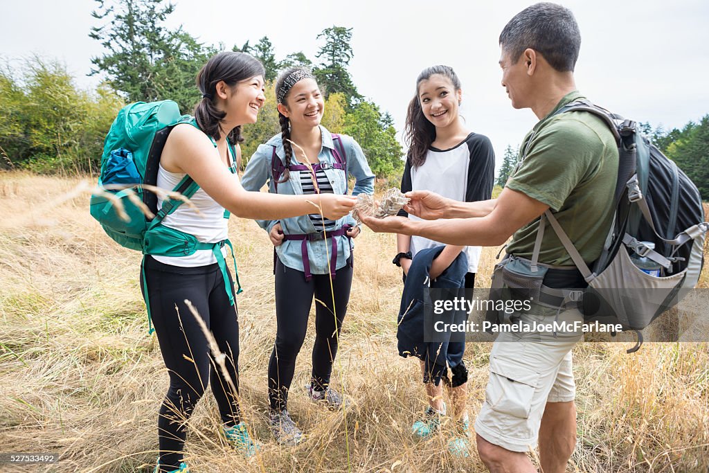 Multi-Generation Family of Hikers Examining Wasp Nest in Grassy Field