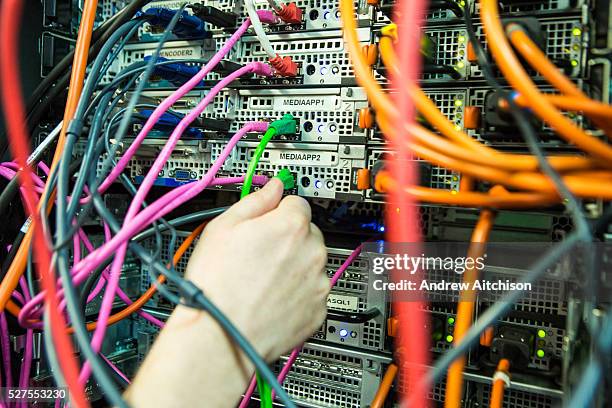 An IT technician adjusts a cable in a server room in a British business office in London, United Kingdom.