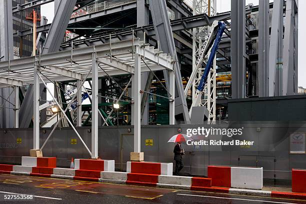 Businessman with corporate umbrella passes beneath a new construction project by Brookfield Multiplex in London's financial district, the Square...