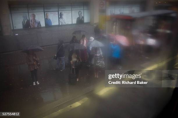 Seen through upper-deck window condensation, a crowd of waiting passengers use umbrellas at a bus stop during damp, gloomy weather in central London....