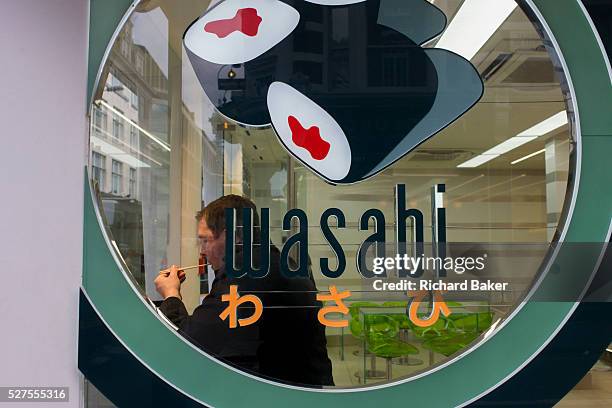 Man eats Wasabi with chopsticks in a central London cafe in Soho. Placing the Japanese food into his mouth, the man deftly uses the wooden eating...