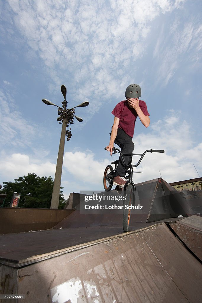 A young man balancing on a BMX bike at the top of a ramp