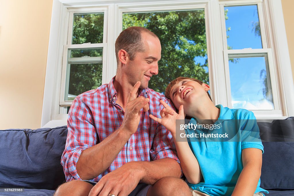 Father and son with hearing impairments signing I Love You in American sign language on couch