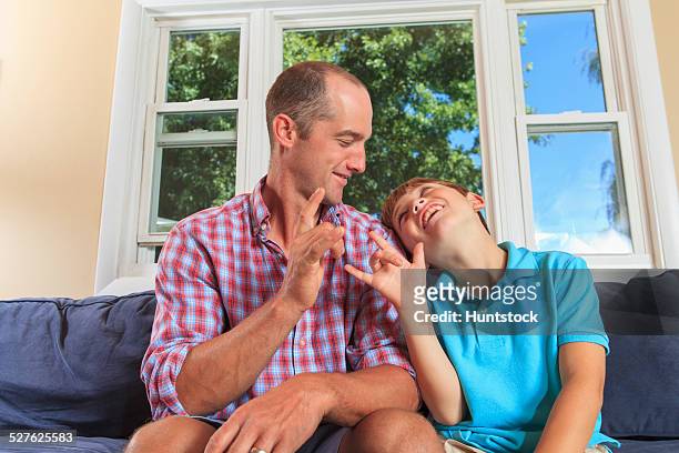 father and son with hearing impairments signing i love you in american sign language on couch - love you stockfoto's en -beelden
