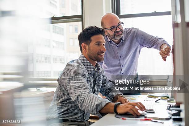 office life. two men in an office, using a computer screen.  - business talk stock pictures, royalty-free photos & images