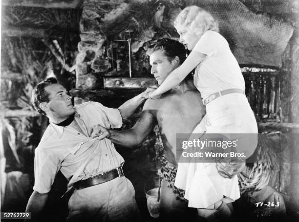 American actor Buster Crabbe , as Tarzan, holds actress Julie Bishop , as Jane, in one hand and threatens actor Edward Woods with the other in a...