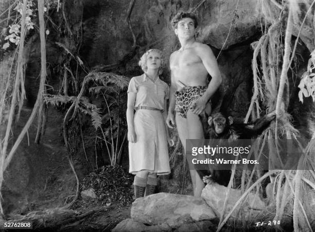 American actors Julie Bishop , Buster Crabbe , and a chimpanzee stand at the mouth of a cave and gaze with determination into the distance in a scene...