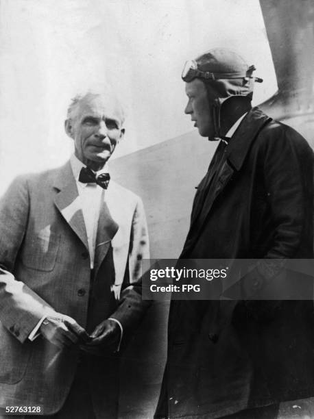 American businessman and automobile manufacturer Henry Ford talks with pilot Charles A. Lindbergh , dressed in a long coat and flight helmet, as they...