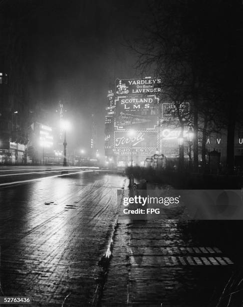 Time-lapsed photograph of a night scene in Leicester Square shows a wide variety of electrically lit billboards and signs advertising many different...