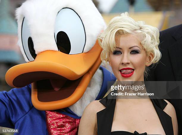 Singer Christina Aguilera poses with Donald Duck in front of the Sleeping Beauty Castle after launching the "Happist Celebration on Earth" during the...