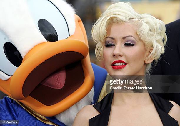 Musician Christine Aguilera and Donald Duck pose in front of the Sleeping Beauty Castle after launching the "Happist Celebration on Earth" during the...
