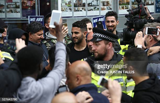 Leicester City's Algerian midfielder Riyad Mahrez is helped to a car as he makes his way through crowds of fans after having lunch with team-mates an...