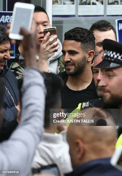 Leicester City's Algerian midfielder Riyad Mahrez reacts as he is helped to a car whilst making his way through crowds of fans after having lunch...