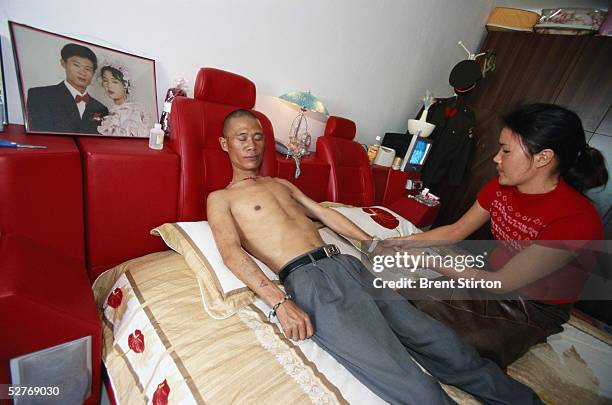 Sickly HIV positive man receives a massage from his HIV positive wife on November 29, 2004 in Ruili, China. The man is a former government official...