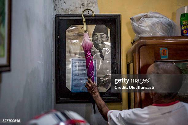 Sukar, 83 years old, a villager who witnessed Indonesia's anti-communist massacre, takes his umbrella off a poster of Indonesia's first President...