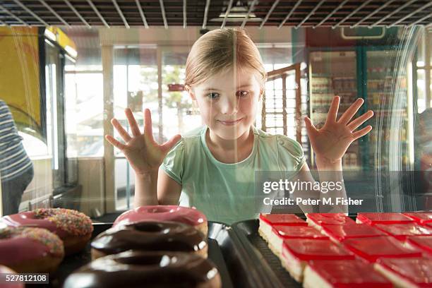 girl (6-7) at bakery looking through cabinet at doughnuts - vitrinekast stockfoto's en -beelden