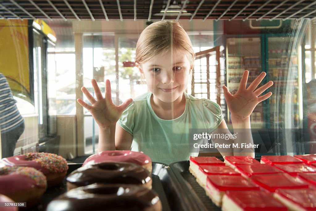 Girl (6-7) at bakery looking through cabinet at doughnuts
