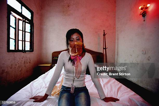 Young underage prostitute sits on a bed in a brothel November 25, 2004 in Cheng Du, China. Her face is covered due to her fear of repercussions if...