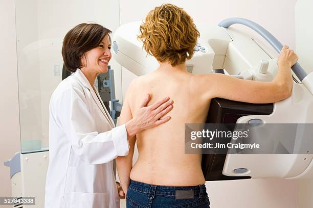 medical technician helping a woman getting a mammogram - mammogram stock pictures, royalty-free photos & images
